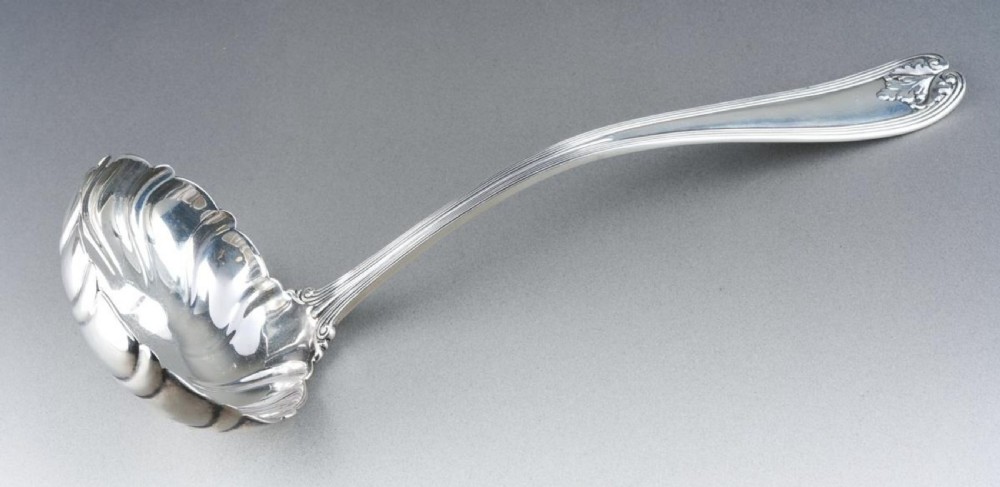 A solid sterling silver soup ladle featuring a curved reeded handle with a scroll motif terminal and a fluted shell-shaped bowl.