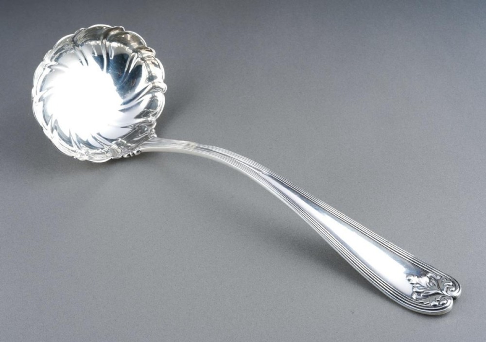 A solid sterling silver soup ladle featuring a curved reeded handle with a scroll motif terminal and a fluted shell-shaped bowl. View III
