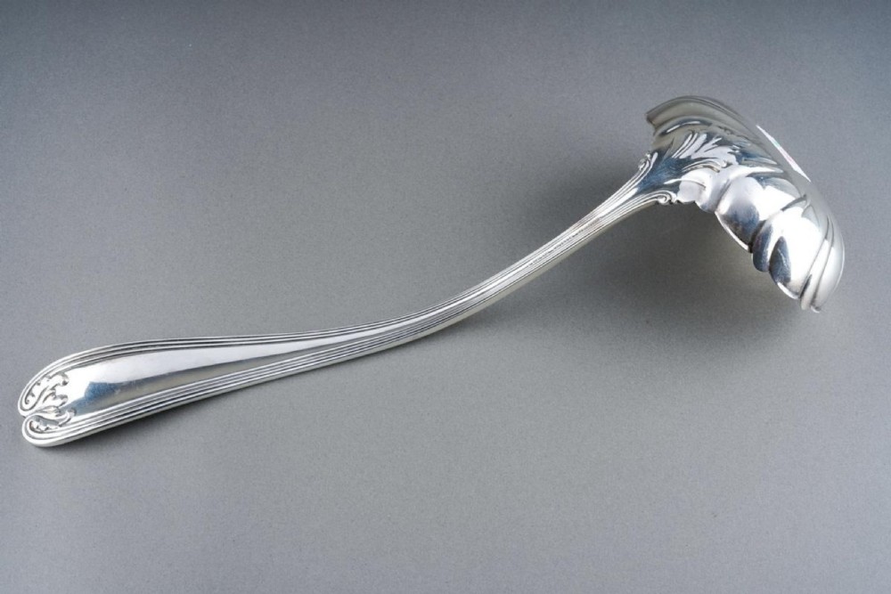 A solid sterling silver soup ladle featuring a curved reeded handle with a scroll motif terminal and a fluted shell-shaped bowl. View IV