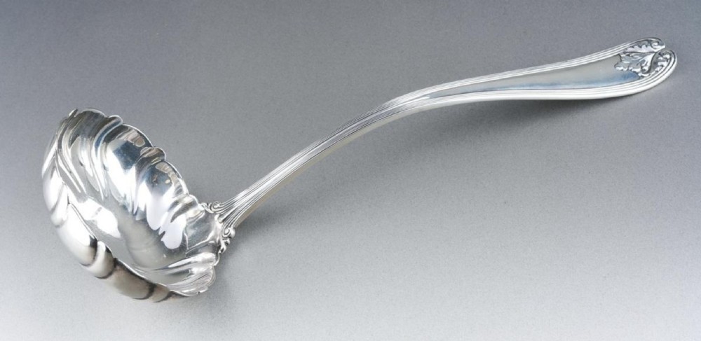 A solid sterling silver soup ladle featuring a curved reeded handle with a scroll motif terminal and a fluted shell-shaped bowl. View VI