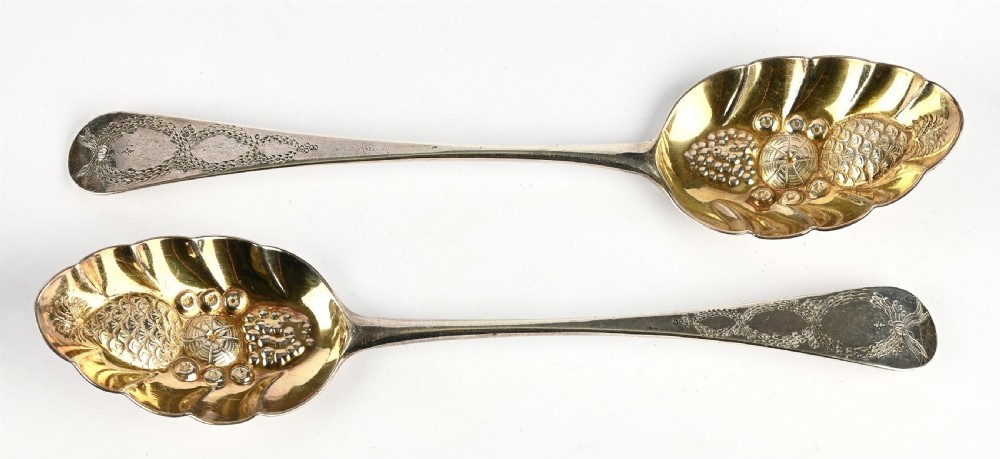 A pair of George III sterling silver berry spoons featuring bright-cut engraved handles and gilt repousse bowls embossed with fruit motifs. View II