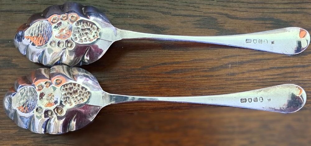 A pair of George III sterling silver berry spoons featuring bright-cut engraved handles and gilt repousse bowls embossed with fruit motifs. View VI