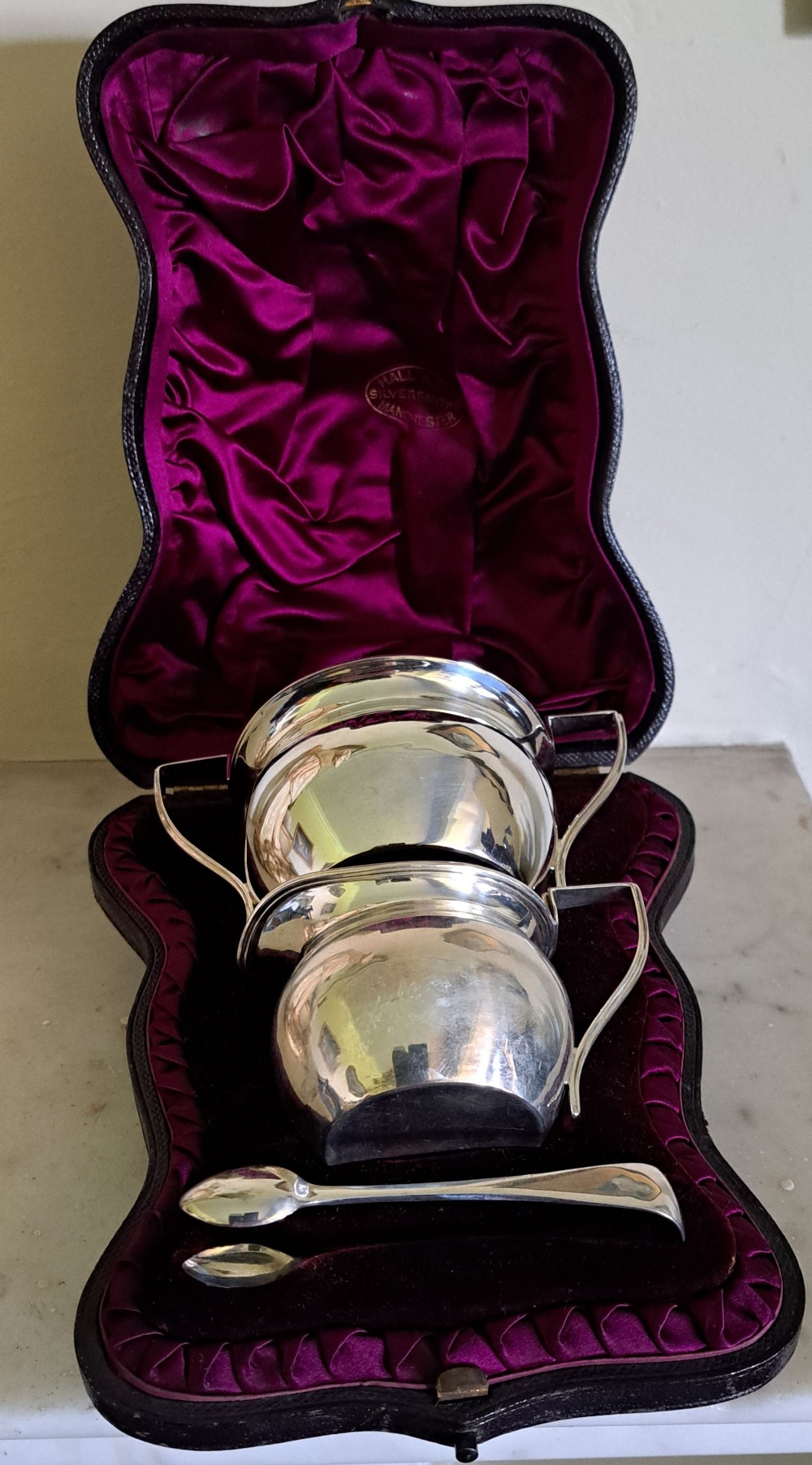 A Victorian silver strawberry set comprising a cream jug, sugar bowl, spoon, and tongs displayed inside a fitted black case lined with deep purple silk and velvet.