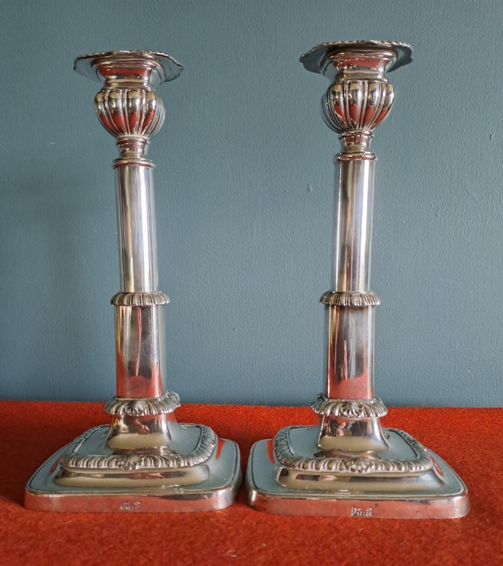 A pair of Victorian silver-plated telescopic candlesticks featuring square weighted bases, ribbed detailing, and adjustable height columns.