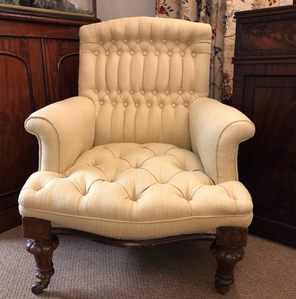 A Victorian button-backed armchair upholstered in cream fabric, featuring turned walnut front legs set on brass castors.