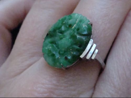 An Art Deco platinum ring featuring a carved oval imperial green jadeite gemstone set with stepped geometric shoulders. View III
