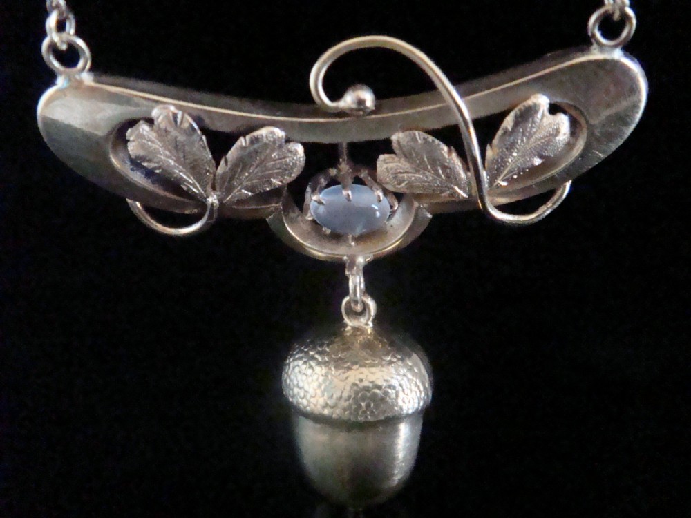 An Art Nouveau yellow gold necklace featuring a central oval moonstone, sculpted leaves, and a textured hanging acorn pendant. View III