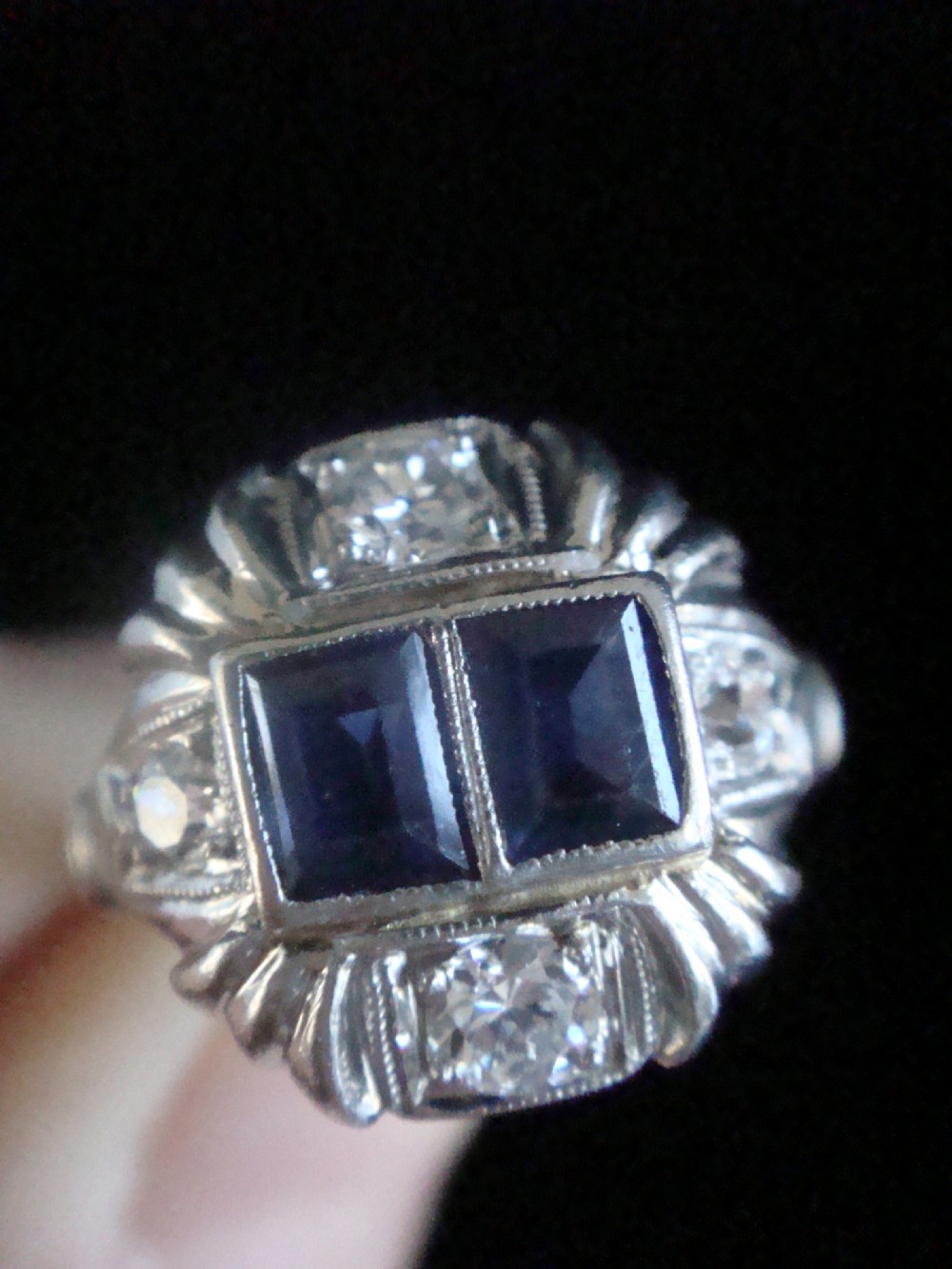 An Art Deco platinum ring featuring two central rectangular blue sapphires flanked by round diamonds and detailed milgrain edging. View II