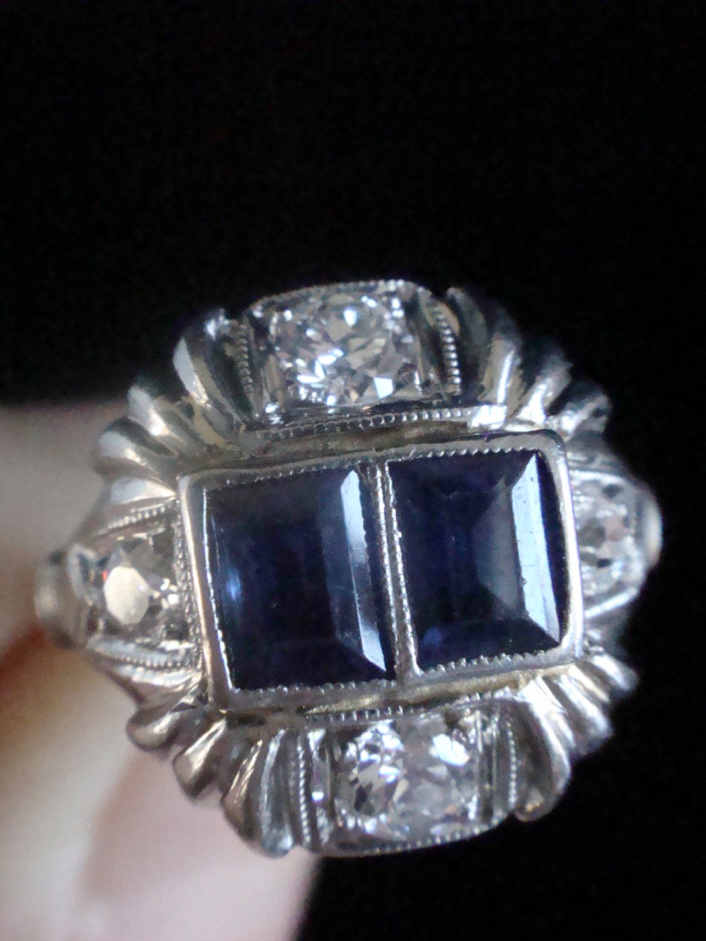 An Art Deco platinum ring featuring two central rectangular blue sapphires flanked by round diamonds and detailed milgrain edging. View IV