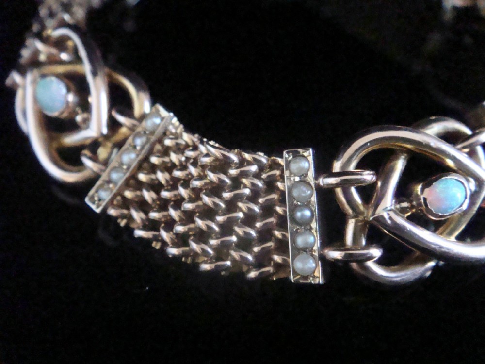 A close-up view of a Victorian nine-carat rose gold bracelet featuring woven mesh links, seed pearl bars, and lovers knot motifs set with cabochon opals.