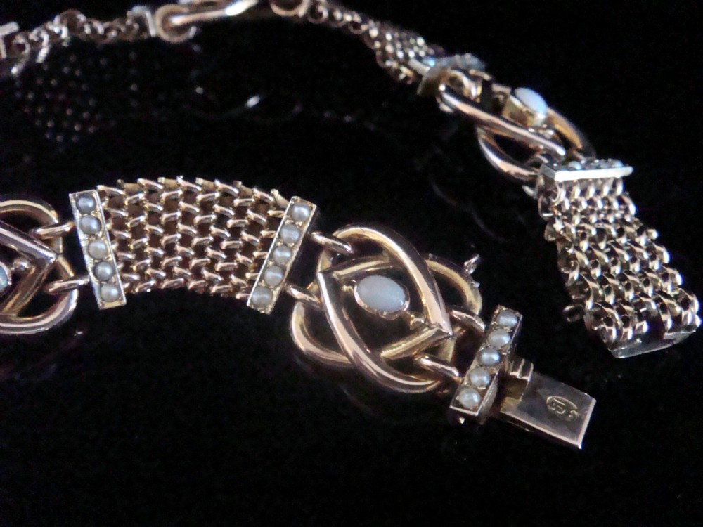 A close-up view of a Victorian nine-carat rose gold bracelet featuring woven mesh links, seed pearl bars, and lovers knot motifs set with cabochon opals. View II