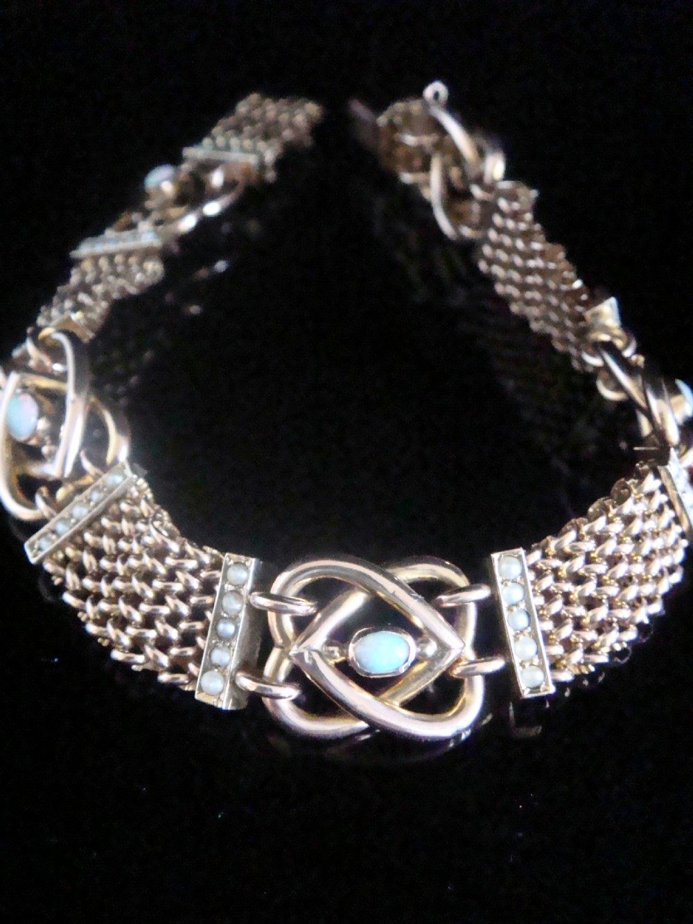 A close-up view of a Victorian nine-carat rose gold bracelet featuring woven mesh links, seed pearl bars, and lovers knot motifs set with cabochon opals. View III