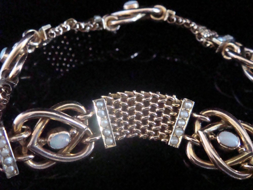 A close-up view of a Victorian nine-carat rose gold bracelet featuring woven mesh links, seed pearl bars, and lovers knot motifs set with cabochon opals. View IV