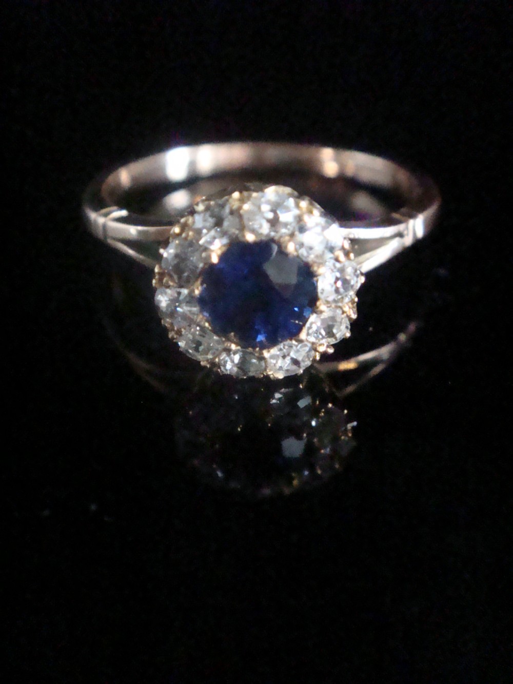 An Edwardian 18ct yellow gold ring with a central round blue sapphire encircled by a halo of old cut diamonds. View II