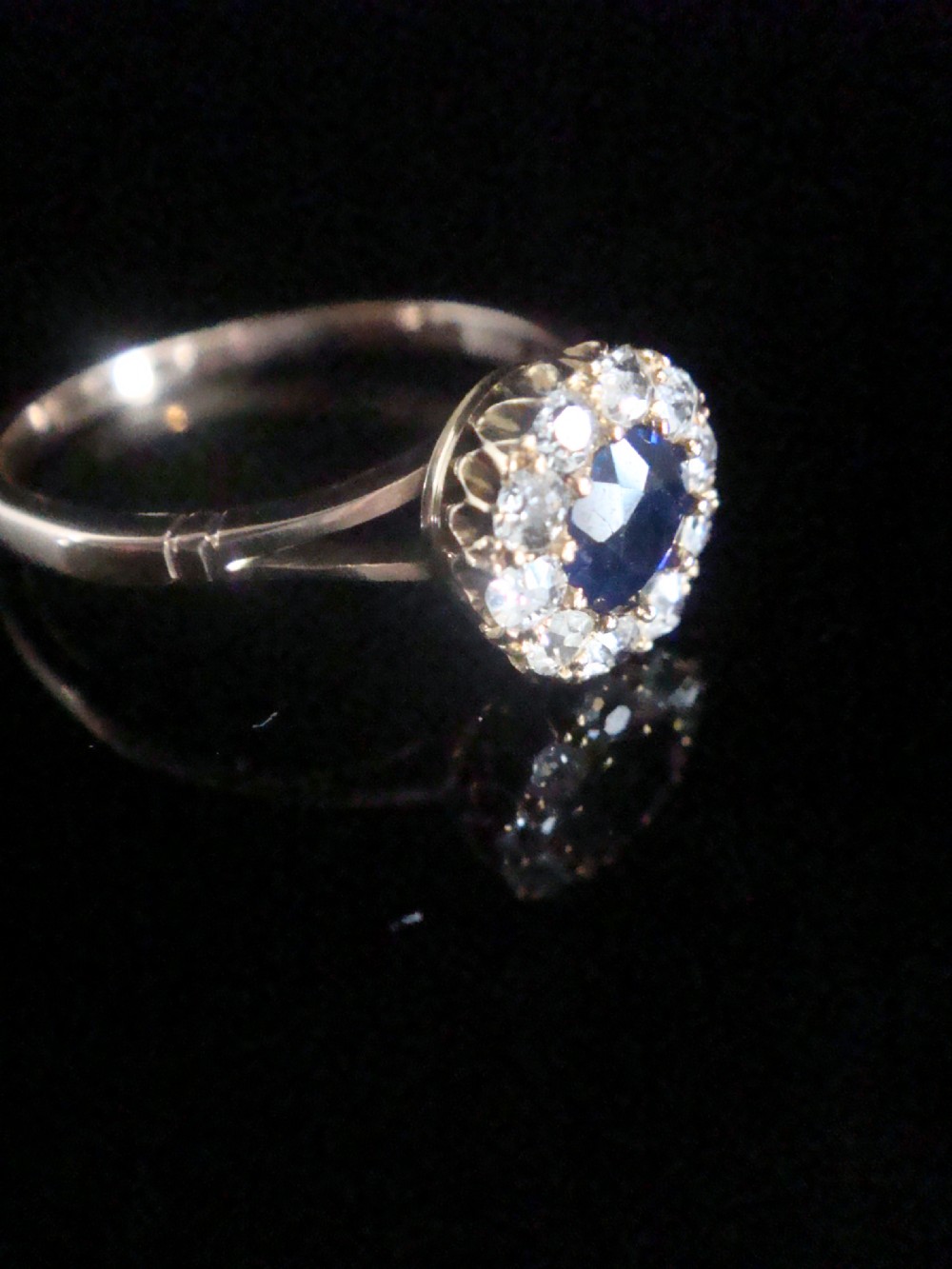 An Edwardian 18ct yellow gold ring with a central round blue sapphire encircled by a halo of old cut diamonds. View III