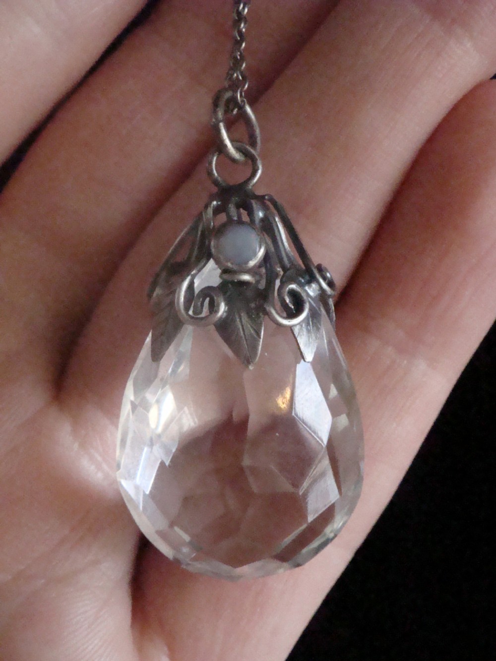An Art Nouveau sterling silver chain necklace featuring a teardrop facetted rock crystal drop accented with an opal cabochon and seed pearls. View III
