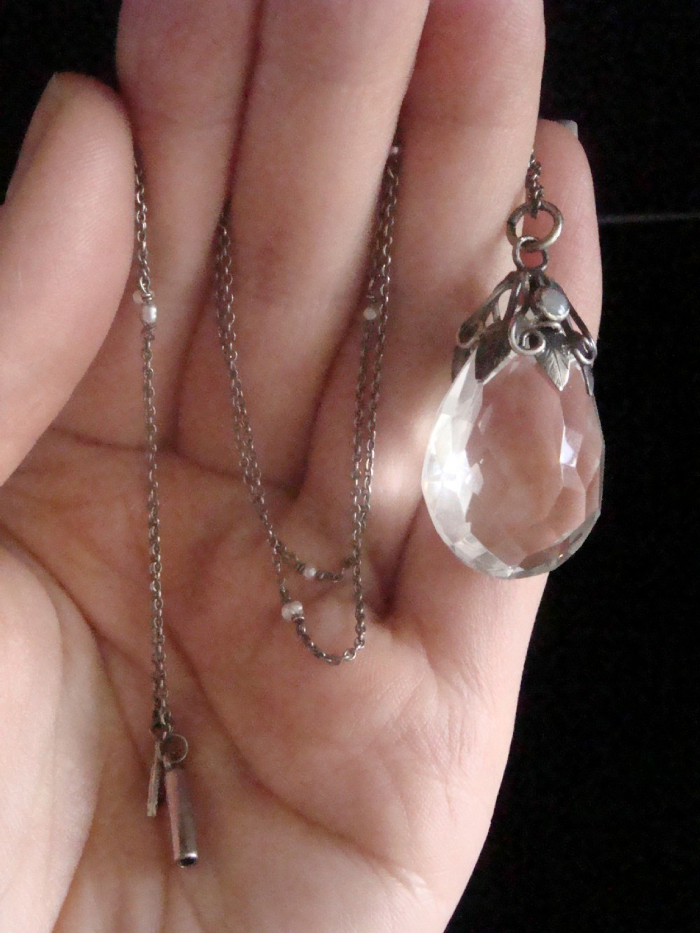 An Art Nouveau sterling silver chain necklace featuring a teardrop facetted rock crystal drop accented with an opal cabochon and seed pearls. View V