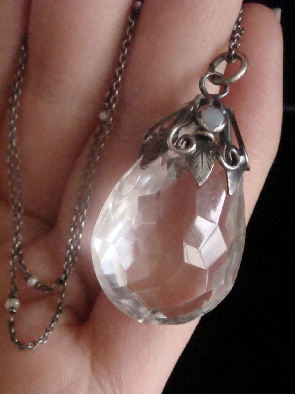 An Art Nouveau sterling silver chain necklace featuring a teardrop facetted rock crystal drop accented with an opal cabochon and seed pearls. View VI