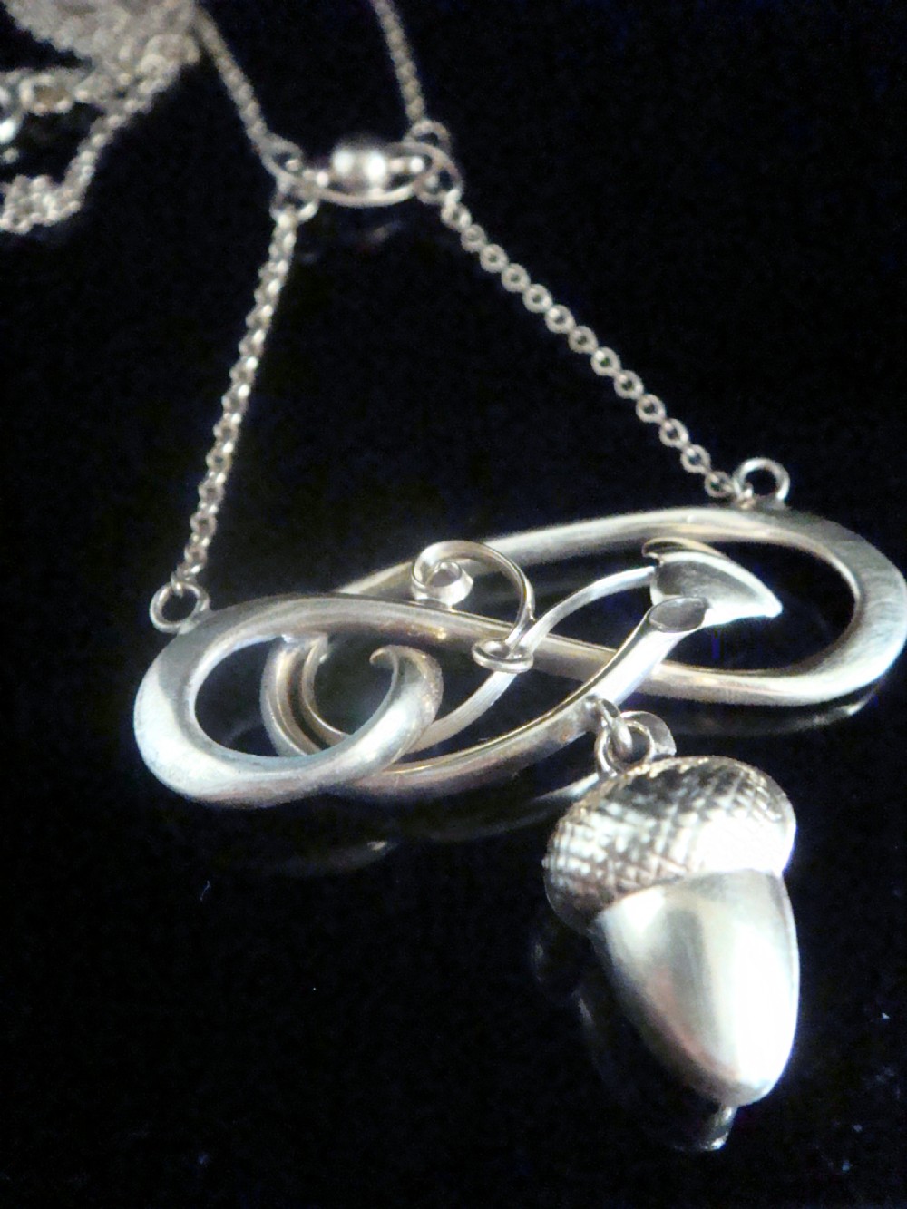 An Art Nouveau yellow gold pendant featuring a sculptural whiplash scroll frame suspending a detailed acorn motif from a fine chain.