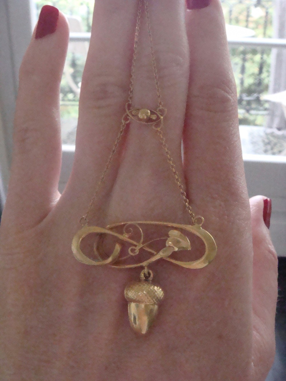 An Art Nouveau yellow gold pendant featuring a sculptural whiplash scroll frame suspending a detailed acorn motif from a fine chain. View IV