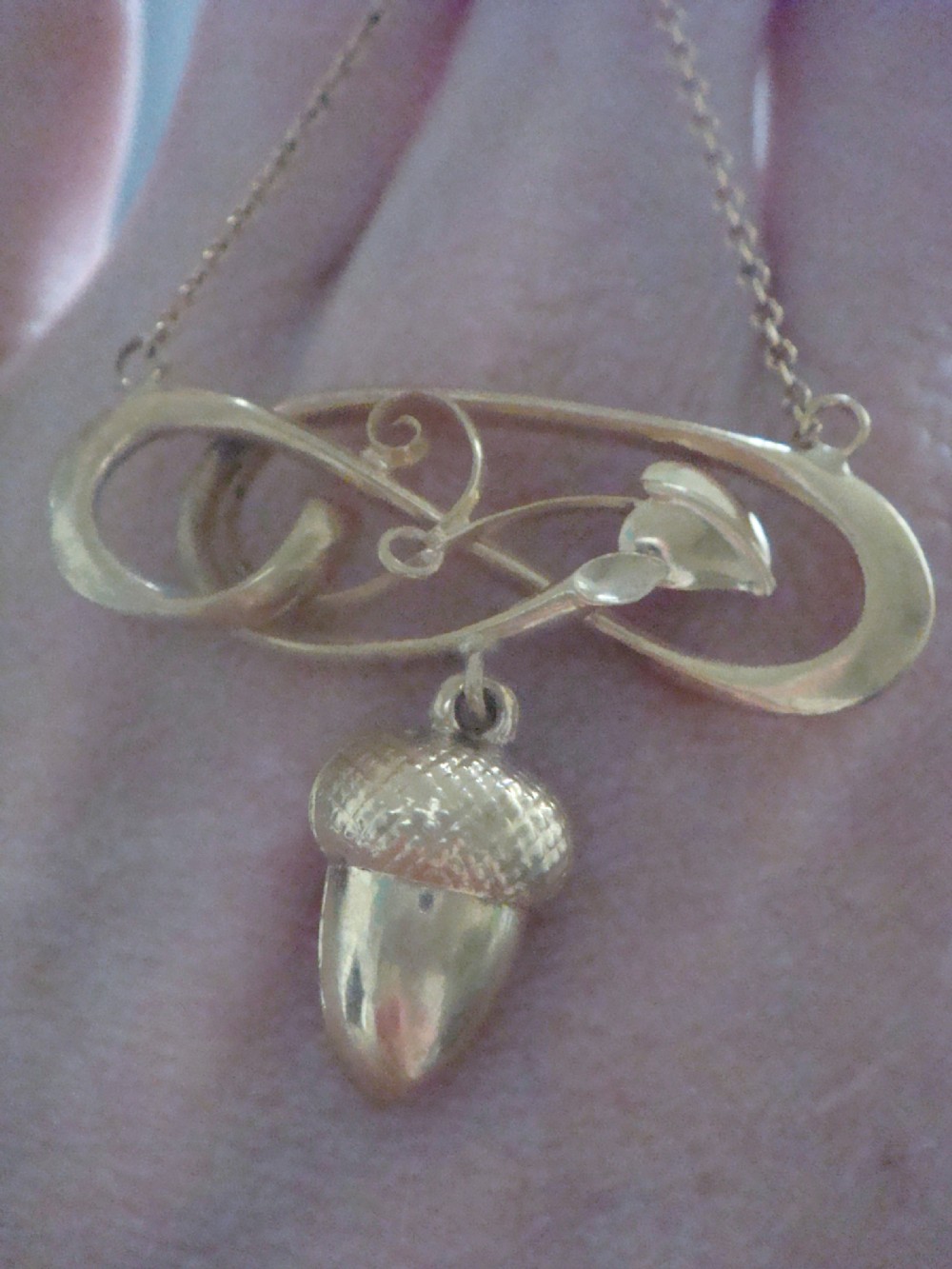 An Art Nouveau yellow gold pendant featuring a sculptural whiplash scroll frame suspending a detailed acorn motif from a fine chain. View V
