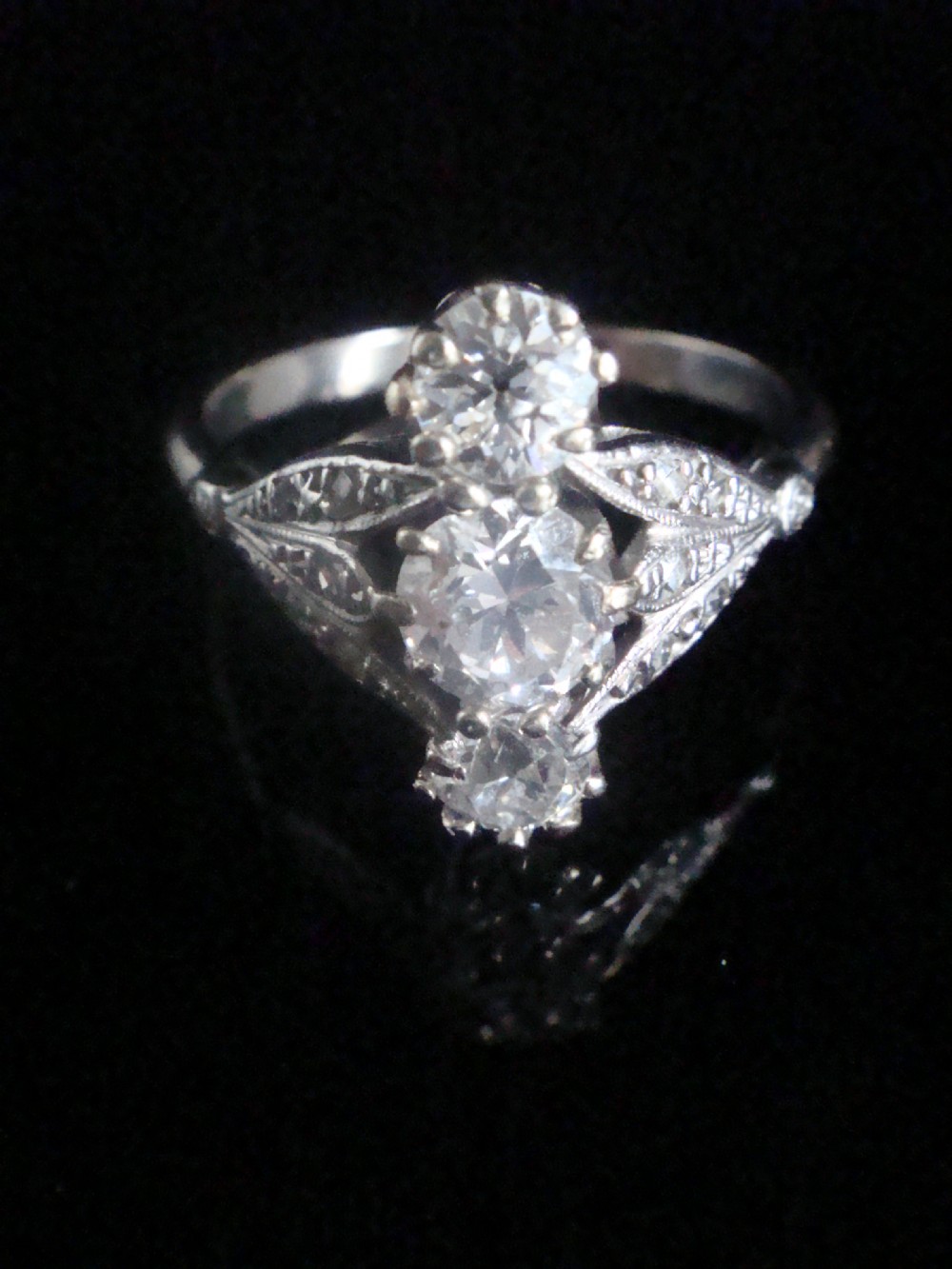 An Edwardian platinum ring featuring three vertically set round old-cut diamonds flanked by milgrain openwork leaf shoulders.