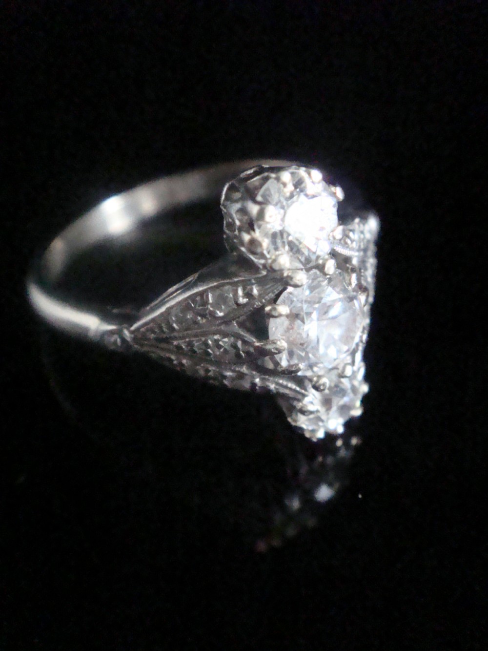 An Edwardian platinum ring featuring three vertically set round old-cut diamonds flanked by milgrain openwork leaf shoulders. View II