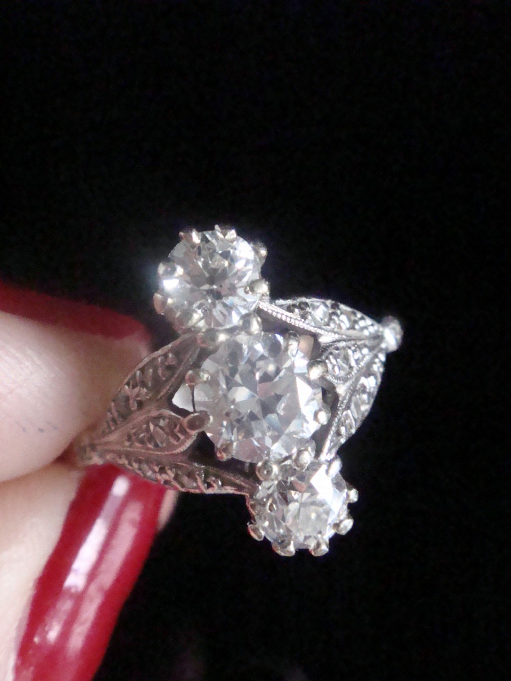 An Edwardian platinum ring featuring three vertically set round old-cut diamonds flanked by milgrain openwork leaf shoulders. View III