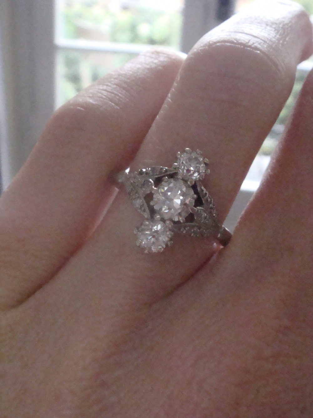 An Edwardian platinum ring featuring three vertically set round old-cut diamonds flanked by milgrain openwork leaf shoulders. View IV