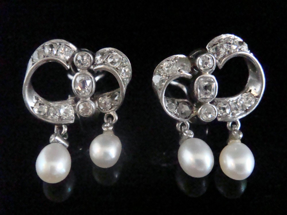 A pair of antique silver bow motif drop earrings set with old-cut diamonds and natural pearl drops. View V