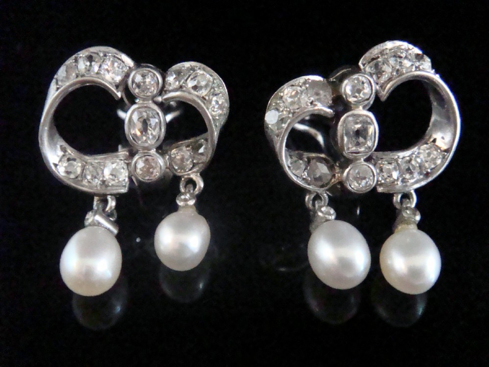 A pair of antique silver bow motif drop earrings set with old-cut diamonds and natural pearl drops.