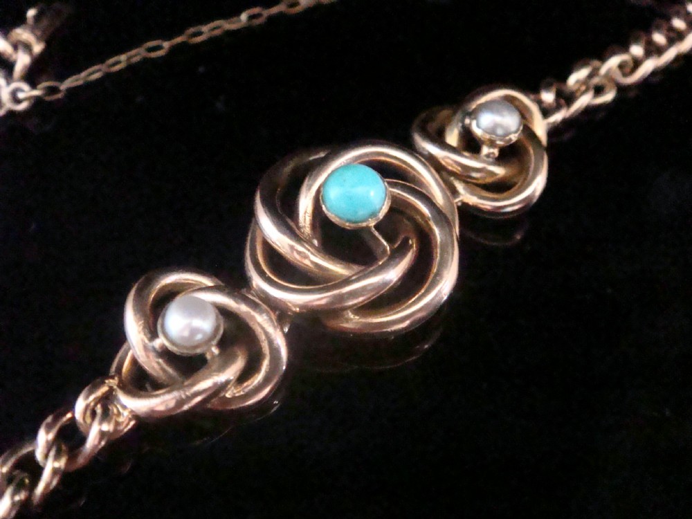 A Victorian 9ct rose gold curb chain bracelet featuring three central lovers knot motifs set with turquoise and seed pearls. View II