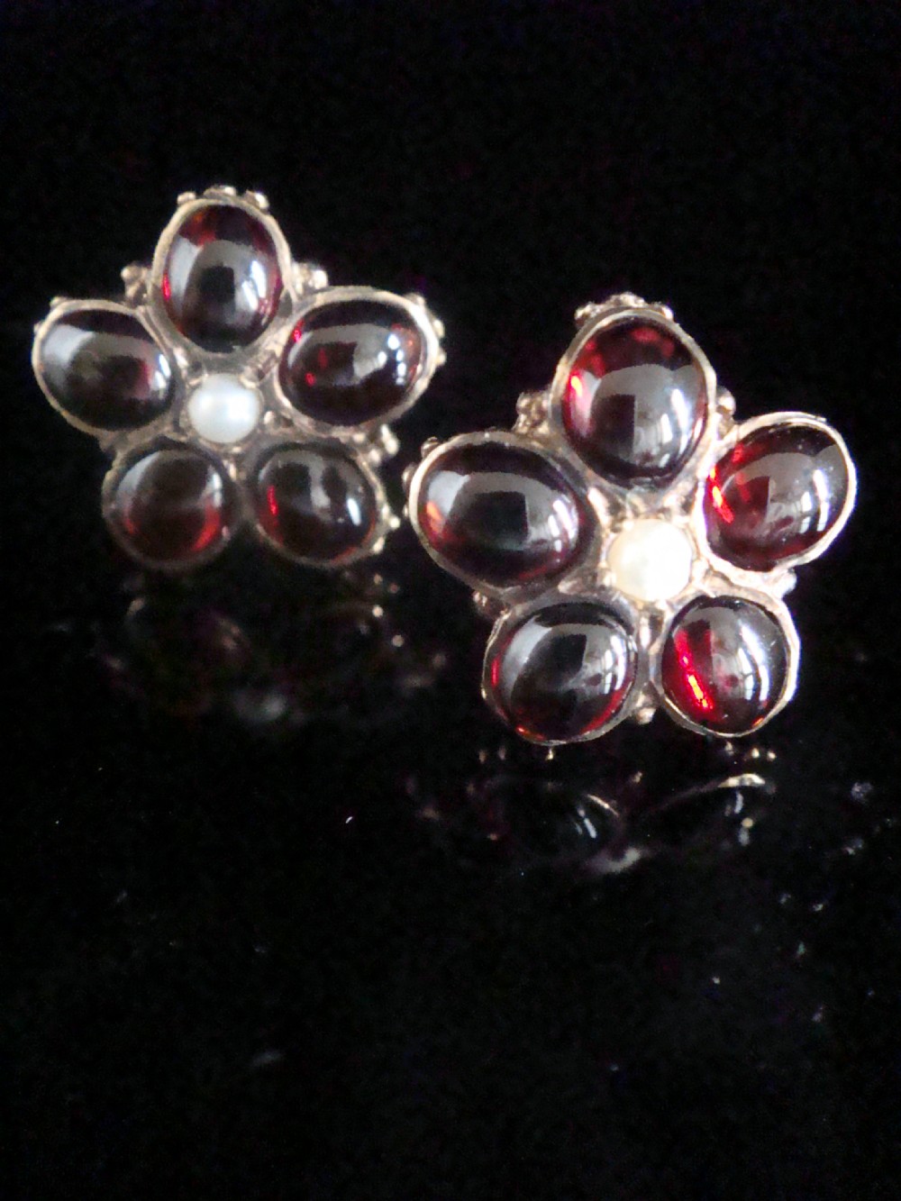 A pair of 1960s flower-shaped stud earrings featuring five smooth cabochon red garnets as petals surrounding a central white pearl, set in gold.