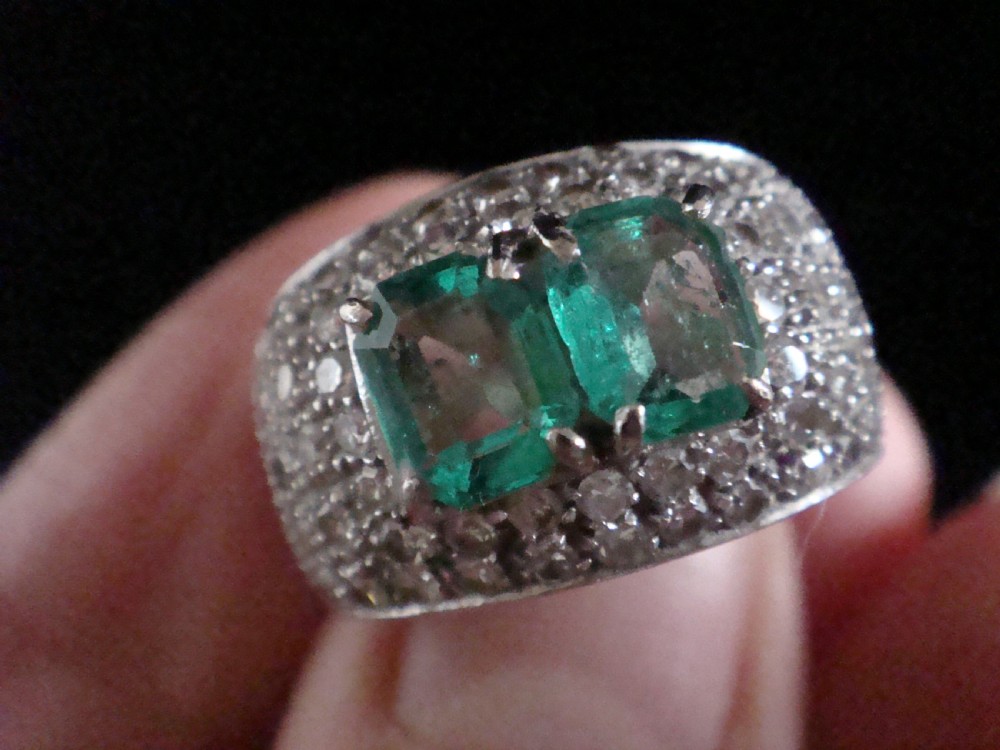 An Art Deco platinum band set with two central emerald-cut green emeralds framed by a broad pave diamond setting. View III