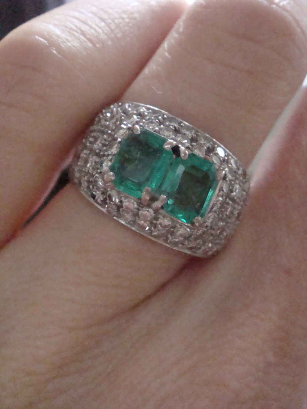 An Art Deco platinum band set with two central emerald-cut green emeralds framed by a broad pave diamond setting. View V