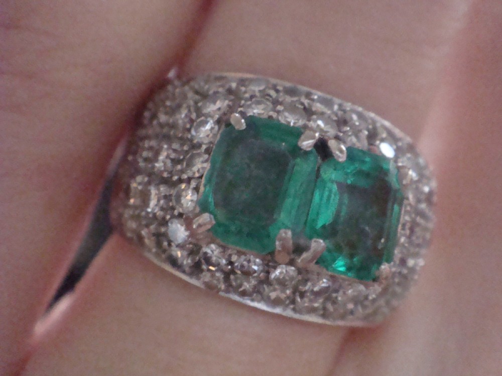 An Art Deco platinum band set with two central emerald-cut green emeralds framed by a broad pave diamond setting. View VII