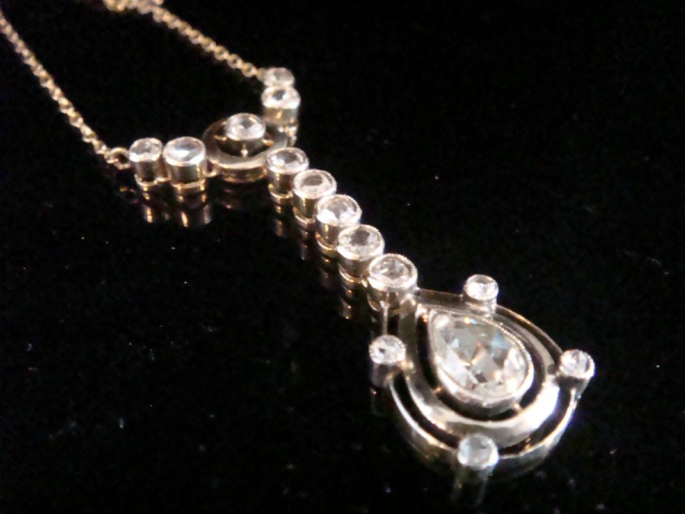 An Edwardian gold link chain supporting an articulated drop pendant set with multiple bezel-set rose cut diamonds terminating in a pear-shaped drop.