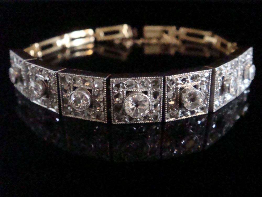 An Art Deco platinum and diamond bracelet composed of square articulated panel links set with central old cut diamonds and millegrain borders.