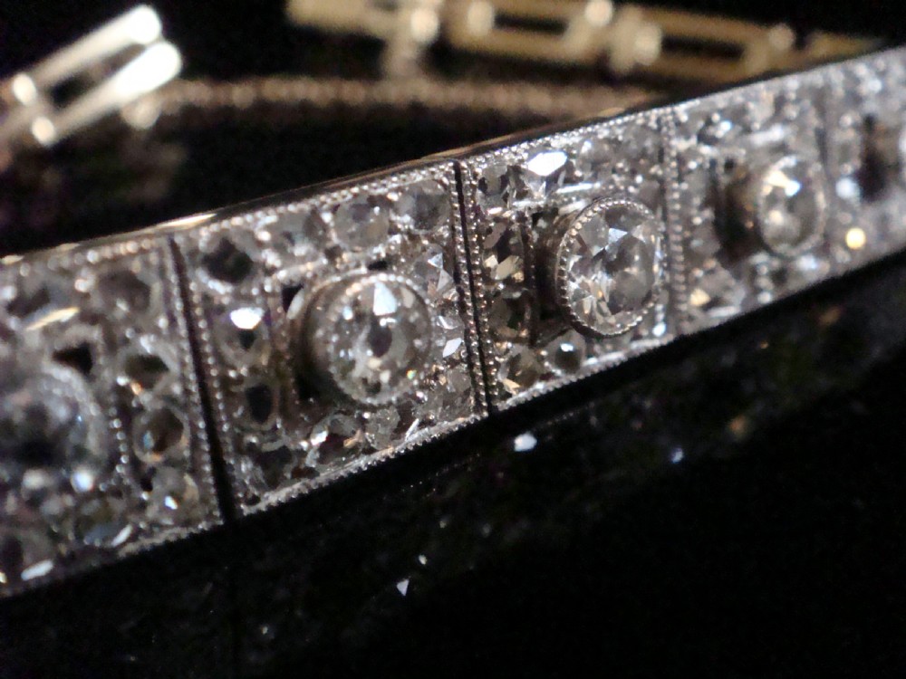 An Art Deco platinum and diamond bracelet composed of square articulated panel links set with central old cut diamonds and millegrain borders. View II