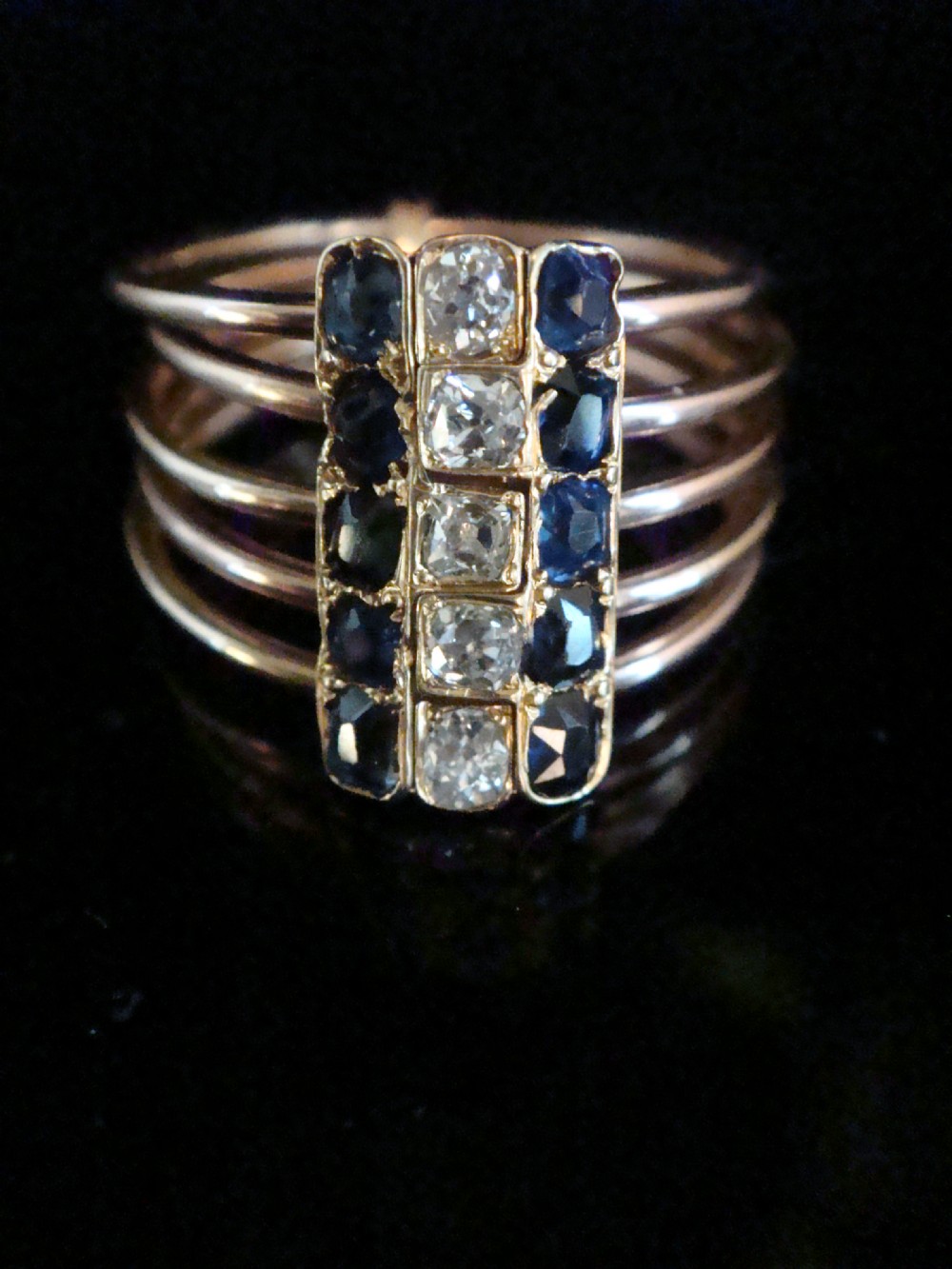 An Edwardian five-row rose gold harem ring featuring a vertical rectangular bar set with central diamonds flanked by blue sapphires.