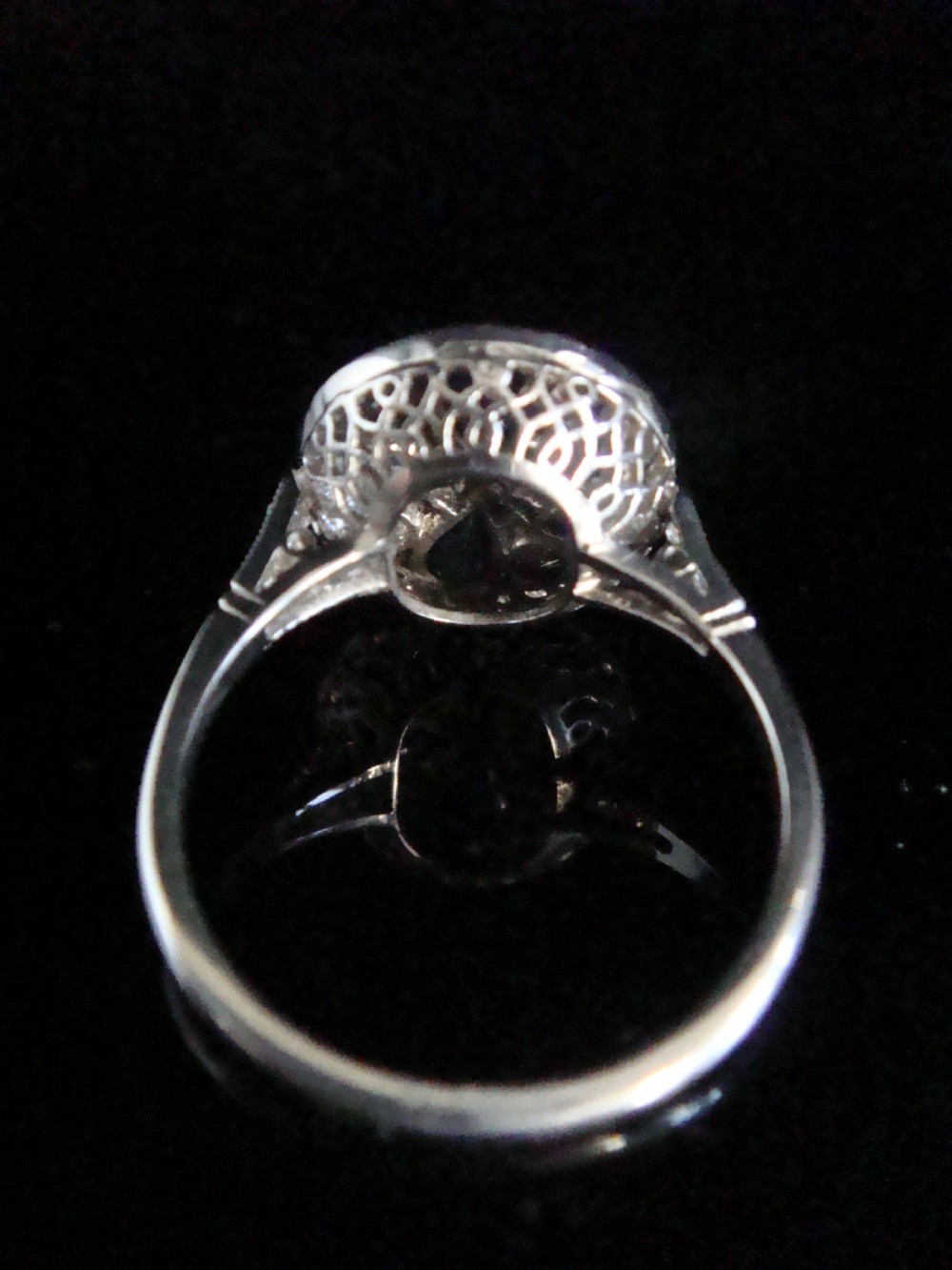 An Art Deco circular platinum ring featuring a central round diamond surrounded by four pear-cut blue sapphires forming a clover motif set amidst pave diamonds. View III