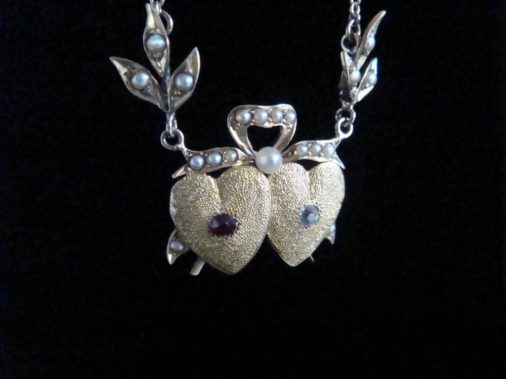 An Edwardian 15ct yellow gold double heart necklace featuring a central ruby, a rose cut diamond, and seed pearl accents on leaf motifs. View III