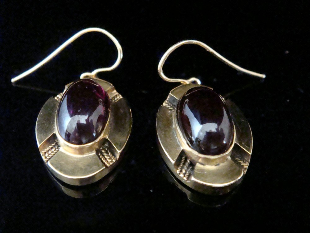 A pair of Victorian 15ct gold drop earrings featuring oval cabochon garnets within textured golden frames with wire hooks. View II