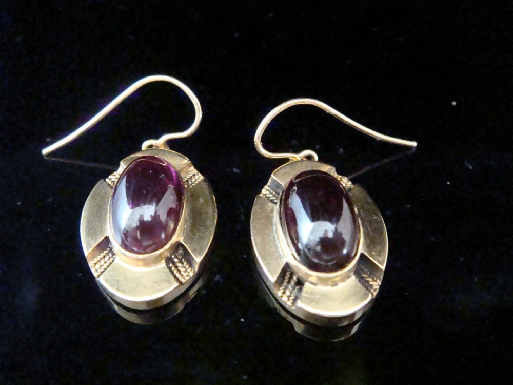 A pair of Victorian 15ct gold drop earrings featuring oval cabochon garnets within textured golden frames with wire hooks. View III
