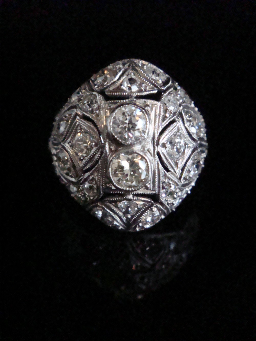 An Art Deco platinum bombe ring set with multiple transitional-cut diamonds in a rounded geometric pattern with millegrain detailing.