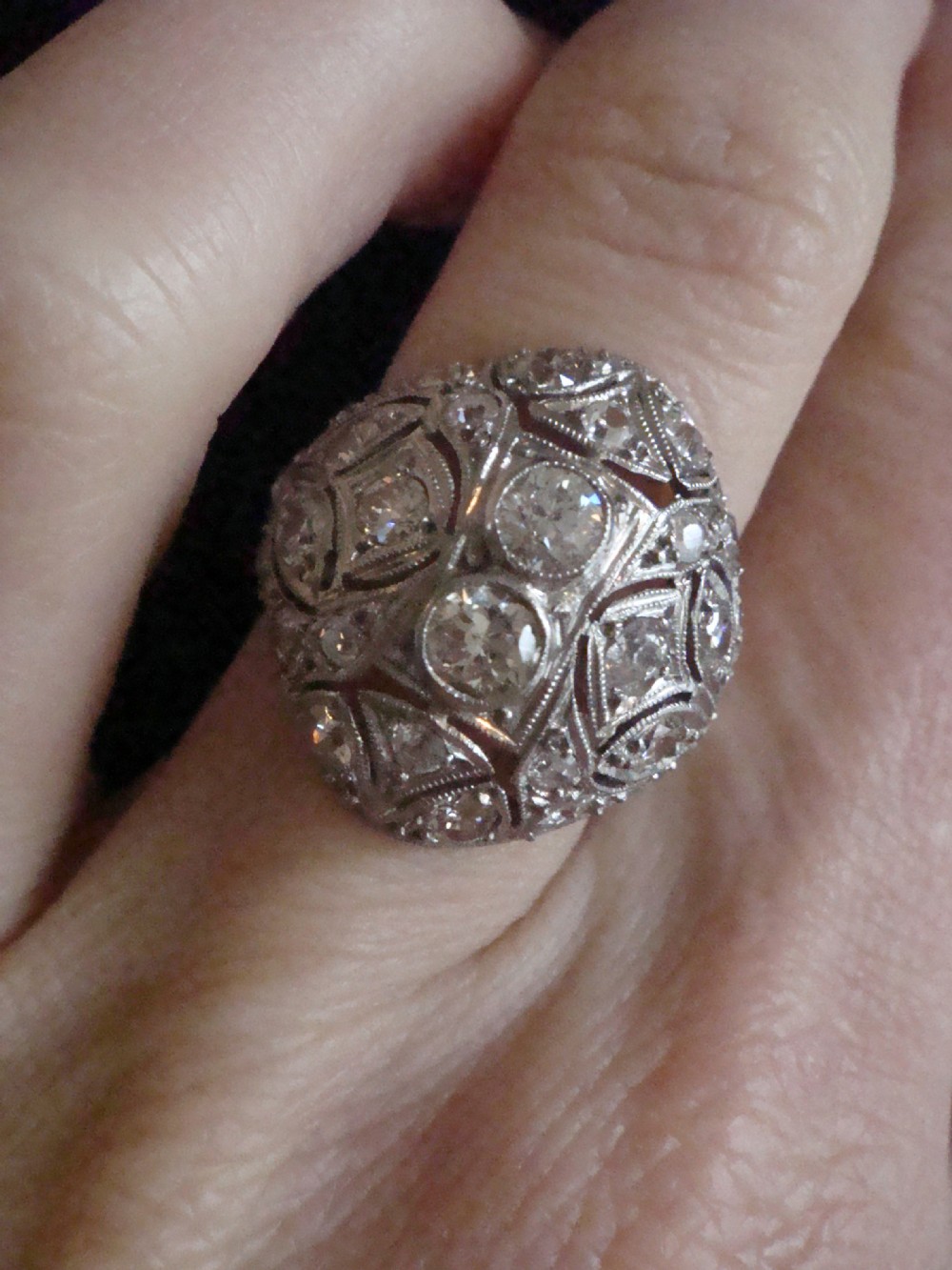 An Art Deco platinum bombe ring set with multiple transitional-cut diamonds in a rounded geometric pattern with millegrain detailing. View III