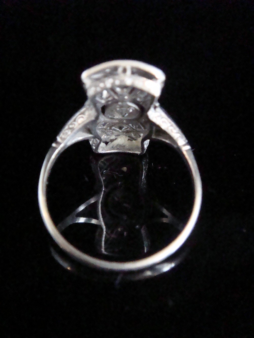 An Art Deco platinum plaque ring featuring a central round diamond set within an elongated geometric frame of smaller diamonds and millegrain detailing. View III