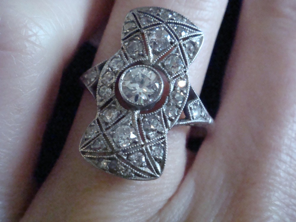 An Art Deco platinum plaque ring featuring a central round diamond set within an elongated geometric frame of smaller diamonds and millegrain detailing. View IV