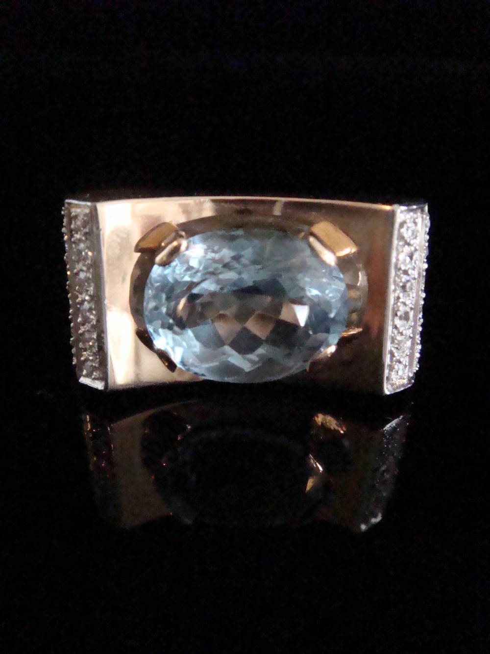 An antique French Tank ring featuring an oval faceted light blue topaz set in gold, framed by broad platinum shoulders set with small accent diamonds.