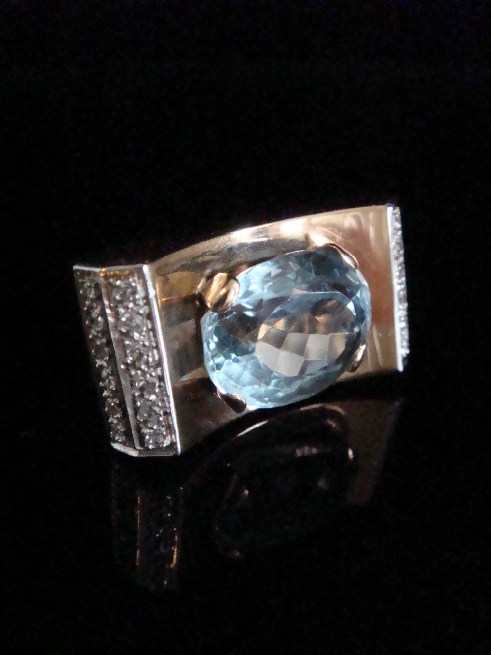 An antique French Tank ring featuring an oval faceted light blue topaz set in gold, framed by broad platinum shoulders set with small accent diamonds. View II